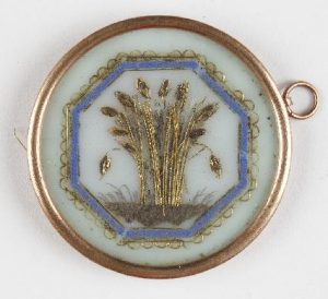  Mediados del S. XIX. Medallón circular de piedra caliza en el que se representa un haz de espigas de trigo. Este haz está realizado con hilos metálicos y cabello inscrito en un marco octogonal pintado en azul y con una orla de metal dorado formando pequeñas ondas.